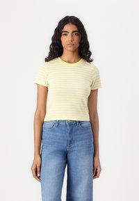 T-shirt à manches courtes rayé jaune et blanc avec un col rond, associé à un jean en denim bleu taille haute. Matière en coton doux.
