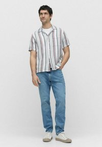 Kortærmet skjorte med knapper og flerfarvede lodrette striber, sammen med lyseblå jeans og hvide sneakers. Fladt, let stof.