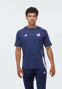 Blå sport-t-shirt med rosa axel-accenter och logotyper. Tillverkad av mjukt tyg, med rund halsringning och korta ärmar.