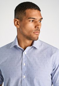 Camicia a righe blu con motivo a pois rossi in contrasto, caratterizzata da un colletto classico e una texture di tessuto liscia.