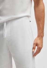 Witte, gestructureerde sportshorts met een koordsluiting in de taille, voorzien van een zijzak en subtiele logo-details op het been.