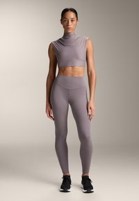 Completo sportivo in malva tenue, composto da un top corto senza maniche con collo alto e leggings a vita alta, realizzati in tessuto liscio ed elastico.