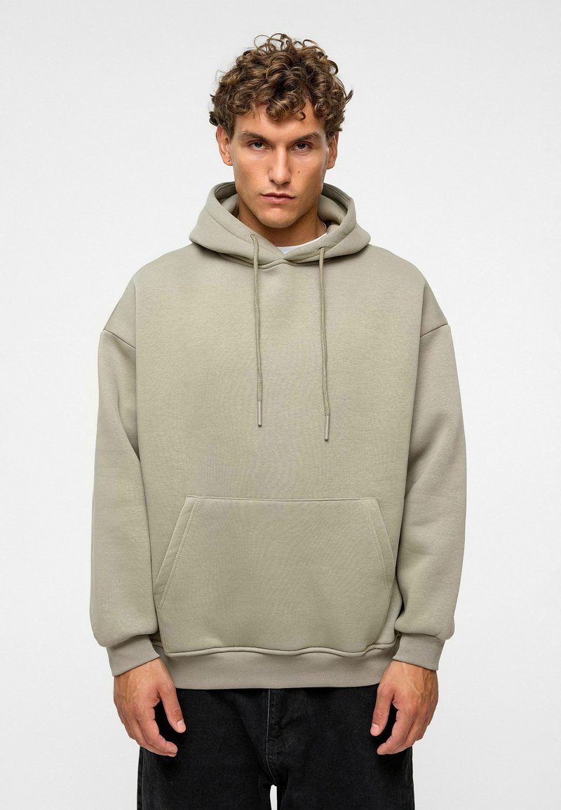 Beige Kapuzenpullover mit einer Fronttasche, Kordeln und Bündchenärmel. Der Stoff hat eine glatte Textur und einen lässigen Schnitt.