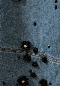 Denimstoff med blå toner, med svarte blomsterpynt, aksenter med skinnende detaljer og synlige sømmer.