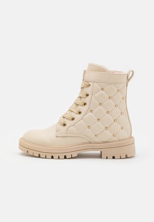 Bottines en simili cuir beige avec des détails matelassés et des clous dorés, dotées d'un laçage et de semelles robustes pour une bonne adhérence.