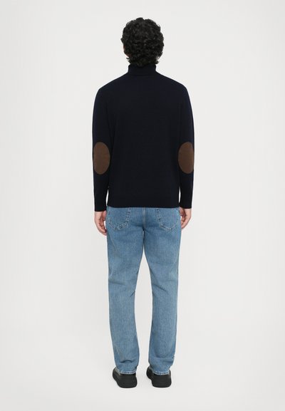 Marineblauwe coltrui met bruine elleboogstukken, gedragen met lichtblauwe jeans, van achteraf bekeken, zachte textuur, relaxte pasvorm.