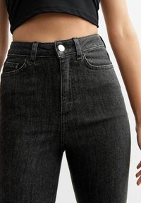 Jean noir taille haute en denim délavé, doté d'une fermeture à bouton, de cinq poches et de passants de ceinture, avec une texture lisse et une coupe droite.