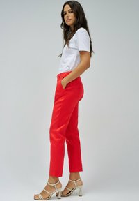 Pantalones rojos ajustados con una textura suave, que cuentan con bolsillos laterales y un diseño de pierna recta, combinados con una camiseta blanca de manga corta y sandalias beige.