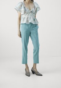 Vaaleansininen, teksturoitu peplum-toppi, jossa on röyhelöhihoja, yhdistettynä mintunvihreisiin housuihin. Harmaat teräväkärkiset korkokengät, joissa on kantakorko.