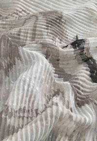 Transluzentes Gewebe mit plissierter Textur in Aquarell-ähnlichen Mustern in Beige-, Grau- und Schwarztönen, akzentuiert durch subtile reflektierende Punkte.