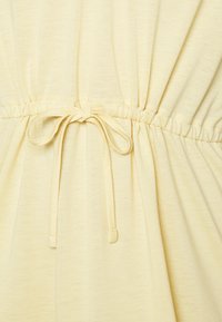 Tecido amarelo claro com uma textura suave, apresentando uma cintura franzida e um detalhe de laço ao centro para ajuste.