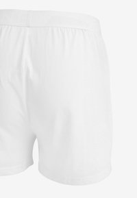Pantalones cortos de algodón blanco con cintura elástica, que presentan letras texturizadas sutiles a lo largo de la cintura y un acabado suave.