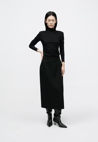 Svart langermet turtleneck-topp kombinert med et svart midikjol med høyt liv, brukt med knelange svarte høye hæler, på en nøytral bakgrunn.