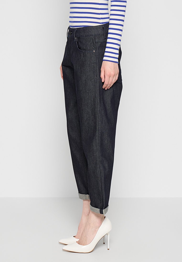 Pantalons en denim foncé avec une coupe décontractée, ourlets retroussés et poches latérales, associés à un haut à rayures à manches longues et des talons hauts blancs.