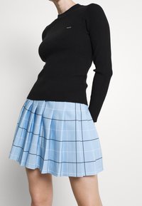 Top negro de manga larga acanalado con cuello redondo, combinado con una falda plisada a cuadros en azul claro con gruesas líneas negras.