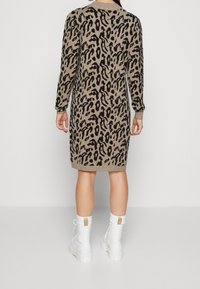 Abito lavorato a maglia beige con motivo leopardato nero, maniche lunghe e polsini a costine. Abbinato a stivali bianchi con suola spessa.