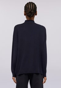 Maglione a maniche lunghe blu navy con taglio rilassato, collo a coste e spacchi laterali. Texture liscia, design casual, abbinato a pantaloni neri.