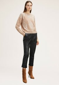 Helles pinkes Paillettenpullover mit Diamantmustern, kombiniert mit eleganten schwarzen Hosen und braunen Knöchelstiefeln. Glatte Texturen, taillierte Passform.