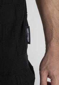 Maglione nero a maglia con tessuto testurizzato, caratterizzato da un orlo a coste e un'etichetta laterale che riporta "Gianni Kavanagh."