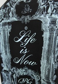 Czarna tkanina z misternym białym wzorem graficznym, napisem "Życie jest teraz" oraz ornamentalnymi wzorami z detalicznymi postaciami i architekturą.