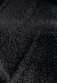 Gros plan d'un tissu polaire noir doux avec une surface texturée et duveteuse, ainsi que de légers plis créant des ombres et de la profondeur.