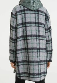 Abrigo de cuadros grises y verdes con un diseño largo, que cuenta con una capucha acolchada de un gris claro y detalles en negro, fabricado en una suave tela texturizada.