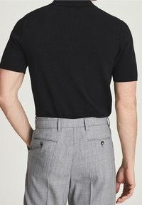 Černé polokošile s krátkým rukávem v kombinaci se šedými texturovanými kalhotami, které mají hladký povrch a jednokorálkovou ozdobu na zadních kapsách.