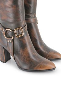 Botas de tobillo de cuero marrón y negro con punta afilada, tacón alto grueso y correa decorativa que cuenta con una hebilla y herrajes en tono dorado.