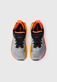 Baskets de trail running grises avec une surface texturée, des lacets noirs, des accents orange et une semelle jaune. Comprend un mesh respirant et des perforations.