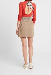 Red ribbed long-sleeve top with a back cutout, paired with a beige mini skirt featuring a patterned waistband. White sneakers complete the look.