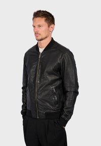 Černá kožená bomber bunda s hladkou texturou, žebrovanými manžetami a límcem. Obsahuje přední zip a boční kapsy. Jednoduchý, klasický design.