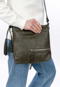 Borsa a tracolla in pelle verde oliva con un accento di nappina, tasca frontale con zip e tracolla regolabile, caratterizzata da una texture liscia.