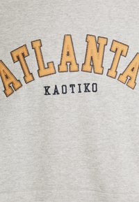 Šedá mikina s nápisem "ATLANTA" ve velkém oranžovém vyšití a menším tmavě modrým textem "KAOTIKO" pod ním. Hladká struktura látky.