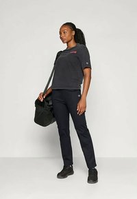 Black cotton t-shirt with short sleeves and red logo, paired with navy pants and black sneakers. Carrying a black duffel bag.