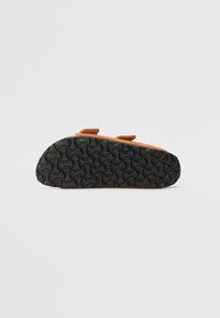 Scarpe in suede color tan con suola in gomma nera sagomata caratterizzata da una trama ondulata; due cinturini regolabili per una migliore vestibilità. Suola progettata per comfort e aderenza.