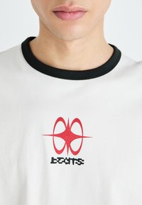 White T-shirt with a black ribbed collar featuring a red graphic design and the word "beats" in a stylized black font.