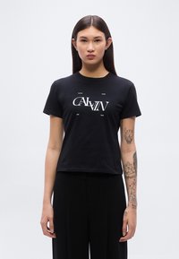 Μαύρο βαμβακερό μπλουζάκι με λευκό γραφικό κείμενο στο κέντρο, κοντά μανίκια και κανονική εφαρμογή. Ομαλή υφή, στρογγυλή λαιμόκοψη.