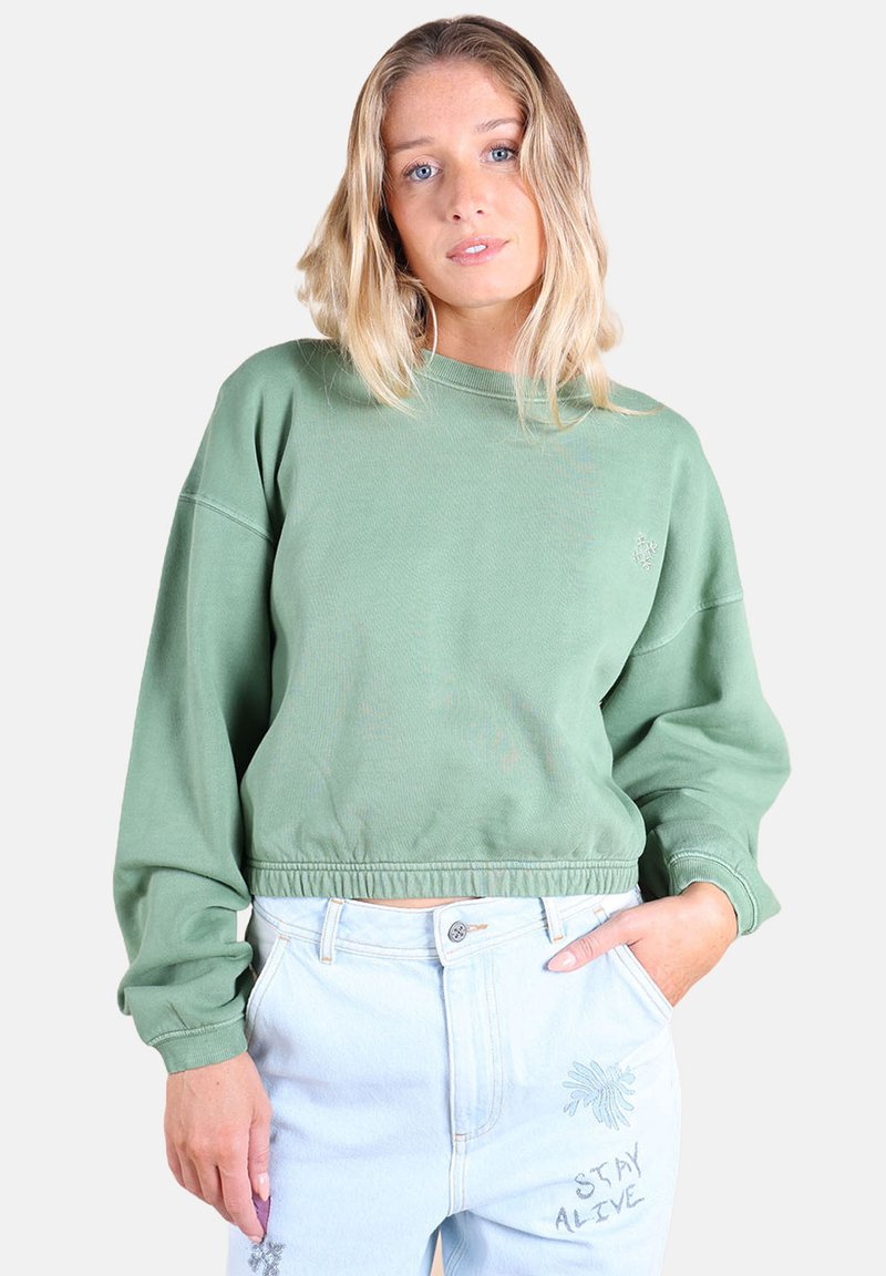 Sweatshirt vert court à manches longues, ourlet côtelé, détails de broderie subtils, associé à un jean bleu clair avec des accents de couture bleus.