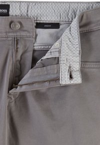 Pantalones elásticos grises con una textura suave, que presentan un cierre frontal con cremallera, botón y una cinturilla estampada.