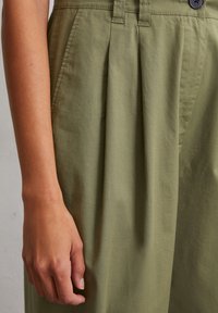 Olijfgroene, hoge taille broek met geplisseerde voorkant, zijzakken en knoopsluiting. Glad, katoenen stof met een subtiele glans.