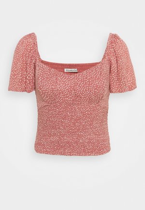 Kurzärmlige Bluse in Rostfarbe mit weißen Polka-Dots, quadratischem Ausschnitt, geraffter Taille und aufgebauschten Ärmeln.
