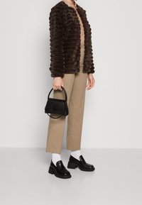 Brun fuskpälsjacka med ribbat mönster, beige vida byxor, svarta klackskor med blockklack och en liten svart handväska med kedjedetalj.