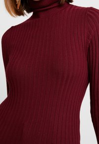 Ribbed turtleneck-neule syvässä burgundinpunaisessa värissä. Ominaisuudet pitkät hihat ja tiukka muotoilu, joka korostaa pehmeää, teksturoitua neulekangasta.