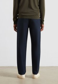Marineblauwe wijde broek van een soepele, lichte stof, gecombineerd met crèmekleurige schoenen en een olijfgroen langemouwen top.