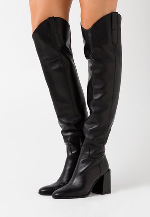 Bottes en cuir noir, hautes jusqu'à la cuisse, au design ajusté, avec un bout pointu et un talon carré. Elles présentent des détails cousus et un bord supérieur haut.