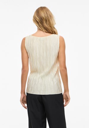 Top sin mangas crema con textura de pliegues verticales, escote redondeado y un corte relajado, combinado con pantalones negros.
