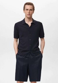 Camicia a maniche corte blu navy con finitura testurizzata, abbinata a pantaloni corti su misura dello stesso colore. Design semplice, con colletto classico e bottoni frontali.