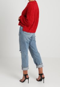 Pull en velours rouge avec des manches surdimensionnées, associé à un jean clair à ourlet et des sandales à talons noirs.