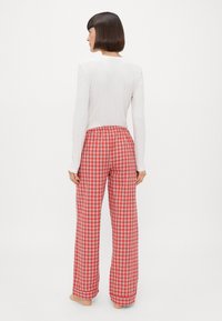 Rode geruite loungebroek met een elastische tailleband, gecombineerd met een aansluitend wit longsleeve shirt. De stof lijkt zacht en lichtgewicht.