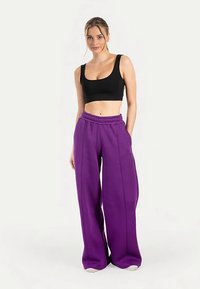 Sort crop top og lilla vidde sweatpants med høj talje. Bukserne har en glat tekstur og sidelommer.